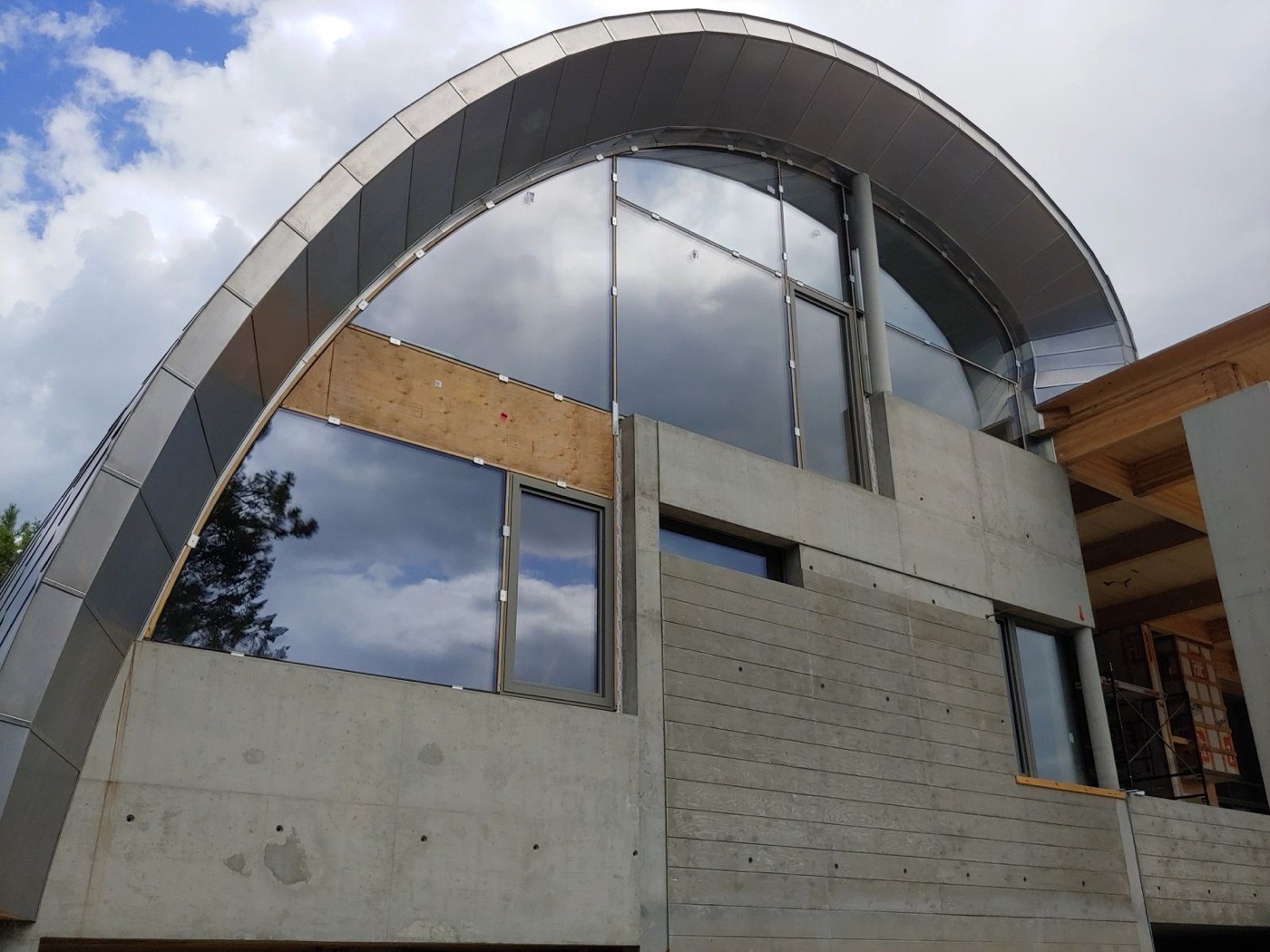 Curved standing-seam metal roof over an arched glass wall on a modern concrete and timber home