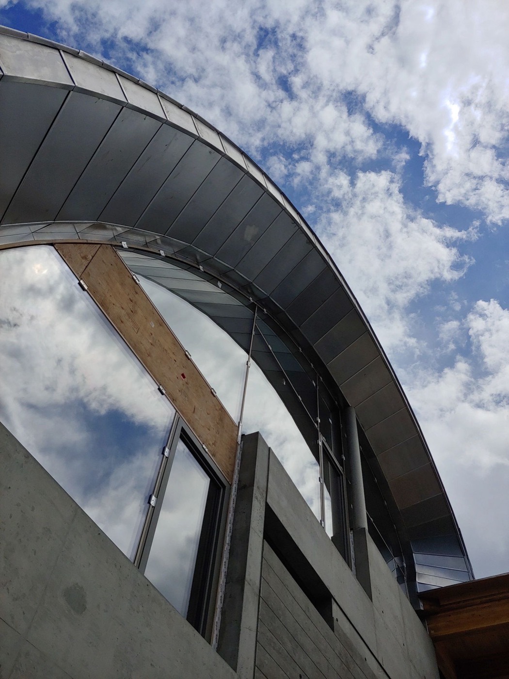 Underside of a curved metal roof edge in flat-lock panels, seen against the sky