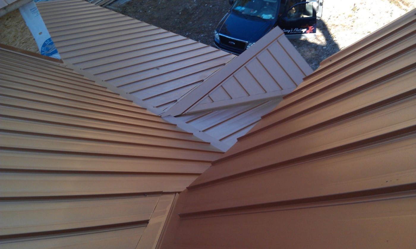 Metal roof panels meeting at hips and a dormer, photographed from the ridge