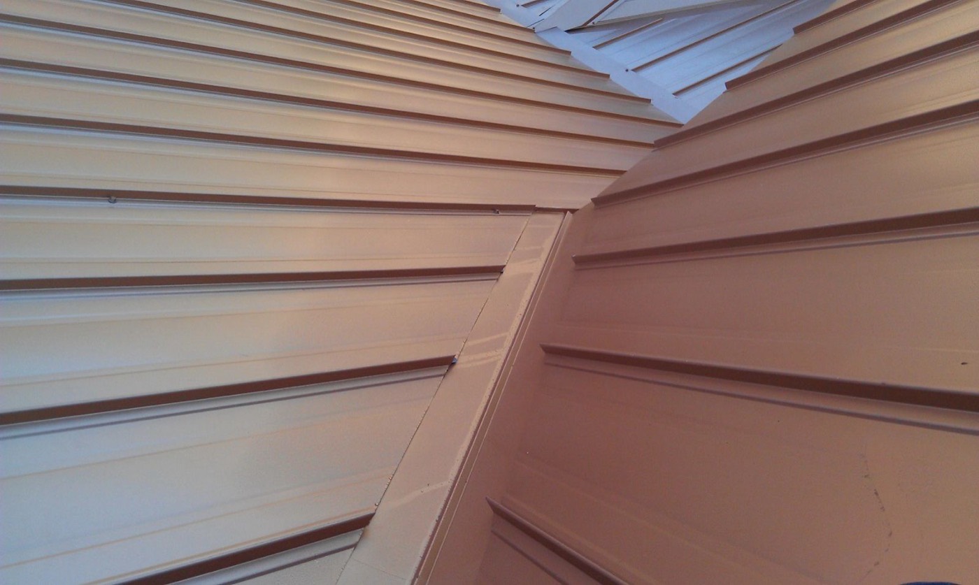 Tan standing-seam metal roof planes meeting at a formed valley junction